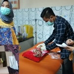 Petugas medis Puskesmas Kadur sedang memeriksa kondisi kesehatan bayi. Inset: Kardus bekas minyak goreng berisi kaos kuning yang berlumuran darah serta kain kafan.