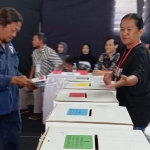 Petugas KPPS (kanan) saat mengarahkan seorang pemilih untuk memasuki surat suara sesuai warnanya (foto: ist)