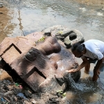Gunawan saat membersihkan arca berbentuk kala (penthul) yang baru ditemukan di Sungai Penthul Dusun Kranggan, Desa Nambaan, Kecamatan Ngasem, Kabupaten Kediri. Foto: Muji Harjita/ BANGSAONLINE.com