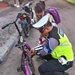 Aipda Ahmad Antoni, Salah satu anggota Unit Turjawali Satlantas Polres Ngawi, saat membetulkan sepeda siswi SD yang berangkat sekolah.