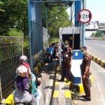 Petugas gabungan memantau penyemprotan disinfektan bagi pengendara motor di pintu masuk jembatan Suramadu, Senin (30/3).