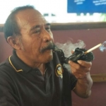 Sartono saat menikmati sebatang rokok dengan sambungan pipa yang diklaim dari Nyi Roro Kidul. foto: YUNIARDI SUTONDO/ BANGSAONLINE