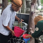 Juru Kunci Sendang Tirto Kamandanu, Mbah Gino, saat menuangkan air yang diambil dari sumber ke wadah milik salah seorang peziarah.