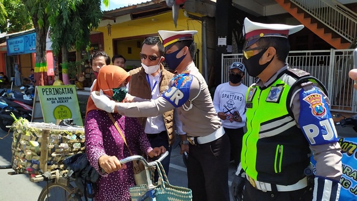 Direktur Utama Bani Group, Ali Zaenal dan Kanit PJR Unit VIII Ditlantas Polda Jatim saat memakaikan masker kain batik kepada seorang pengguna jalan yang melintas di jalan Pamekasan, Kamis (23/4/2020).