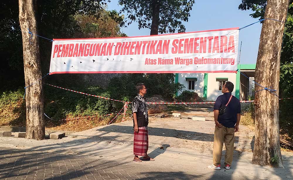 Ketua RW 2 Desa Gulomantung Muhammad Shofiudin dan Agus menunjukkan spanduk yang dipasang warga di depan bangunan Klinik Pratama MWC NU Kebomas. Foto: SYUHUD/ BANGSAONLINE