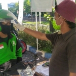 Driver Ojol sedang dicek suhu tubuh dengan thermo gun oleh petugas. 