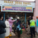 Petugas gabungan sedang mengecek suhu tubuh salah satu pengunjung pasar.