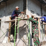 Satgas TMMD bersama warga gotong royong melakukan pengecoran dan melapisi semen pada dinding bangunan.