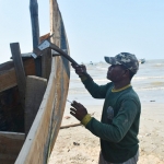 Tak diperbolehkan melaut, salah satu nelayan di Tuban memanfaatkan waktu dengan memperbaiki perahunya.