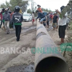 Kesal karena kerusakan jalan Betoyo-Pecuk Manyar tak kunjung diperbaiki, warga memblokir jalan dengan melintangkan pipa gas PGN. foto: syuhud/bangsaonline