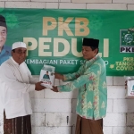 KH. Drs. M. Jamhuri menyerahkan sumbangan sembako dan masker kepada salah satu tokoh masyarakat Arosbaya, Ustadz Farosdad.