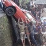 Kondisi mobil sedan yang terperosok saat berusaha dievakuasi oleh warga.