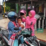 Salah satu ibu bhayangkari saat memakaikan helm kepada bocah yang dibonceng. foto: GUNAWAN/ BANGSAONLINE