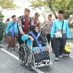 Salah satu calon jemaah haji dari Kabupaten Kediri saat dibantu petugas untuk menuju bus yang akan membawanya ke Surabaya. Foto: Ist