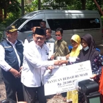 Wakil Ketua IV Baznas Jatim, KH Husnul Khuluq, saat menyerahkan bantuan secara simbolis kepada salah satu mustahik. Foto: Ist