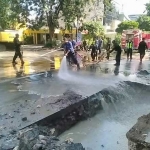 Tim dari pemkot membersihkan lumpur yang meluber ke tengah jalan. 