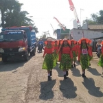 Aktivitas truk muat hasil tambang juga membuat jalan berdebu. Tampak peserta karnaval di samping truk yang mengangkut hasil tambang.