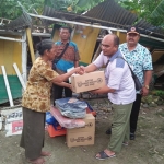 Kastini (60), warga Desa Widang, Kecamatan Widang, Kabupaten Tuban saat menerima bantuan. Tampak latar belakang rumahnya yang roboh diterjang angin puting beliung.