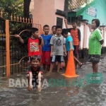 Anak-anak berjaga di depan sekolahnya yang terendam banjir luapan sungai Sadar. foto: YUDI EP/ BANGSAONLINE