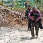 Prada Sugiarto dan Serka Tajib bahu membahu menggendong warga Desa Dompyong yang sakit.