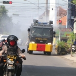 Para personel Polres Kediri Kota sedang beraksi melakukan penyemprotan disinfektan ke jalan raya.