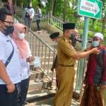 Kepala UPT Destinasi Wisata Terpadu Kawasan Gresik Disparbud Gresik, Sudarmanto, saat mengenakan masker kepada pengunjung Wisata Religi Sunan Giri. Foto: SYUHUD/BANGSAONLINE