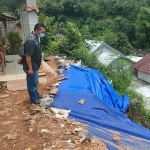 Kondisi tanah retak yang telah ditutupi terpal sebagai antisipasi longsor. Tampak beberapa rumah penduduk di bawahnya. foto: MUJI HARJITA/ BANGSAONLINE