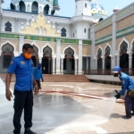 Para petugas sedang menyemprot masjid dengan cairan disinfektan.