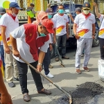 Para kader DPC Partai Gerindra Jember bahu membahu menambal jalan berlubang pakai aspal.