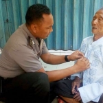 Bhabinkamtibmas Bripka Purnomo saat memberikan santunan baju koko ke seorang pengemis di Pasar Babat Lamongan.
