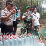 Petugas menunjukkan arak siap edar yang diproduksi di tengah hutan Desa Ngino. foto: GUNAWAN WIHANDONO/ BANGSAONLINE