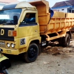 Pekerja proyek pengurukan membersihkan roda truk yang hendak melintas di jalan lingkungan.