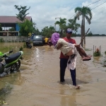 Tampak seorang warga yang menggendong keluarga mereka yang lansia karena tidak mungkin melalui genangan air banjir. 
