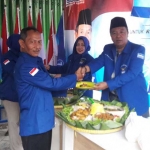 Ketua DPC PD Gresik Eddy Santoso saat menyerahkan tumpeng kepada Arif Rosyidi, kader baru. foto: SYUHUD/ BANGSAONLINE