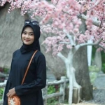 Seorang pengunjung berpose dengan latar belakang pohon sakura di Wisata Kampoeng Toron Samalem.