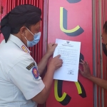 Kasatpol PP Trenggalek saat menempelkan surat seruan dari Bupati Trenggalek ke salah satu warung makan. (foto: HERMAN/ BANGSAONLINE)