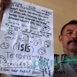 Petugas Polsek Tenggarang saat menunjukkan bukti tulisan dukungan kepada ISIS yang diduga ditulis oleh BN. foto: sugiyanto/ BANGSAONLINE