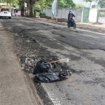 Salah satu lubang di Jalan Raya Oro-Oro Ombo ditandai oleh warga dengan kresek dan tongkat kayu. 