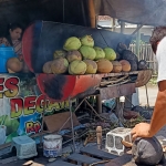 Purwanto saat mengupas degan (kelapa muda) yang sudah dibakar. (foto: MUJI HARJITA/ BANGSAONLINE)