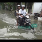 Warga melintasi jalanan yang masih terendam banjir di Desa Rejoagung, Kecamatan Ploso, Kabupaten Jombang, Jumat (13/1). foto: RONY S/ BANGSAONLINE