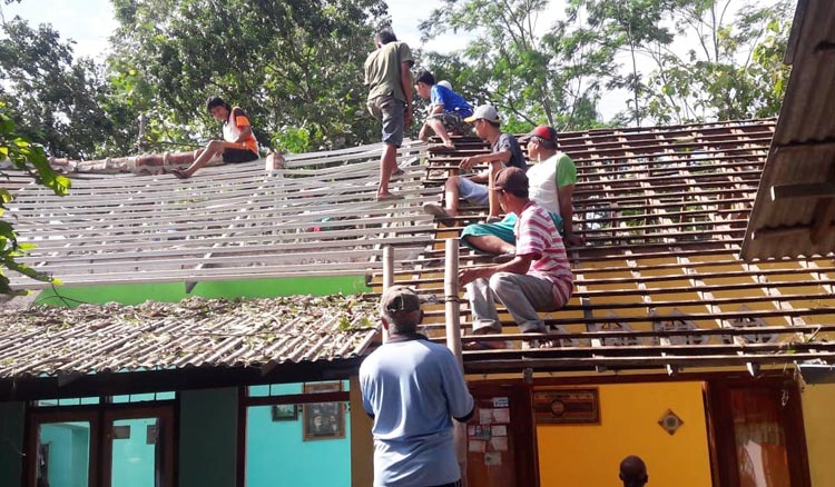 Warga dan petugas BPBD Blitar saat memperbaiki salah satu atap rumah warga.