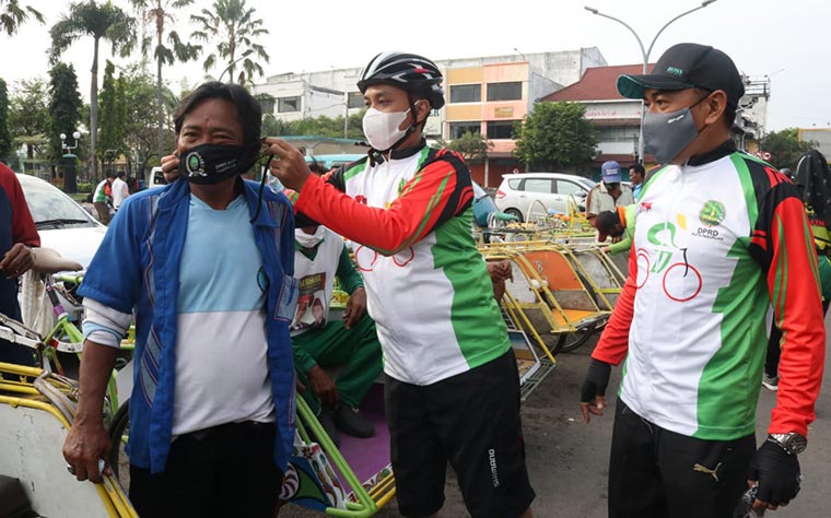 Dewan saat memakaikan masker ke salah satu abang becak dalam kegiatan gowes.