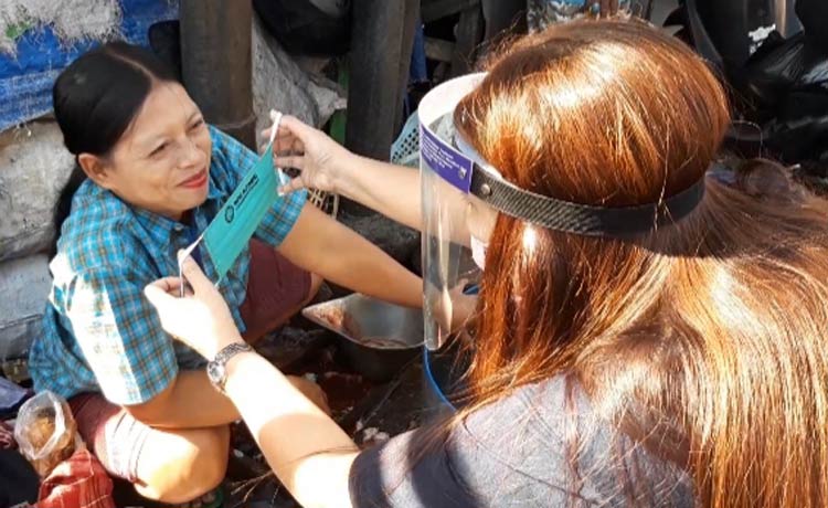 Koordinator RGR, Irma Yulianti, saat akan memakaikan masker kepada salah satu pedagang pasar. (foto: MUJI HARJITA/ BANGSAONLINE)