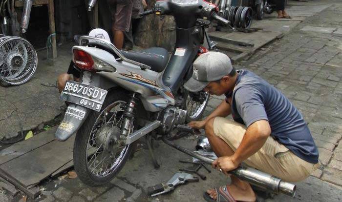 Seorang pedagang mengganti knalpot motor pelanggan di sebuah toko onderdil sepeda motor bekas. (ft: tempo)