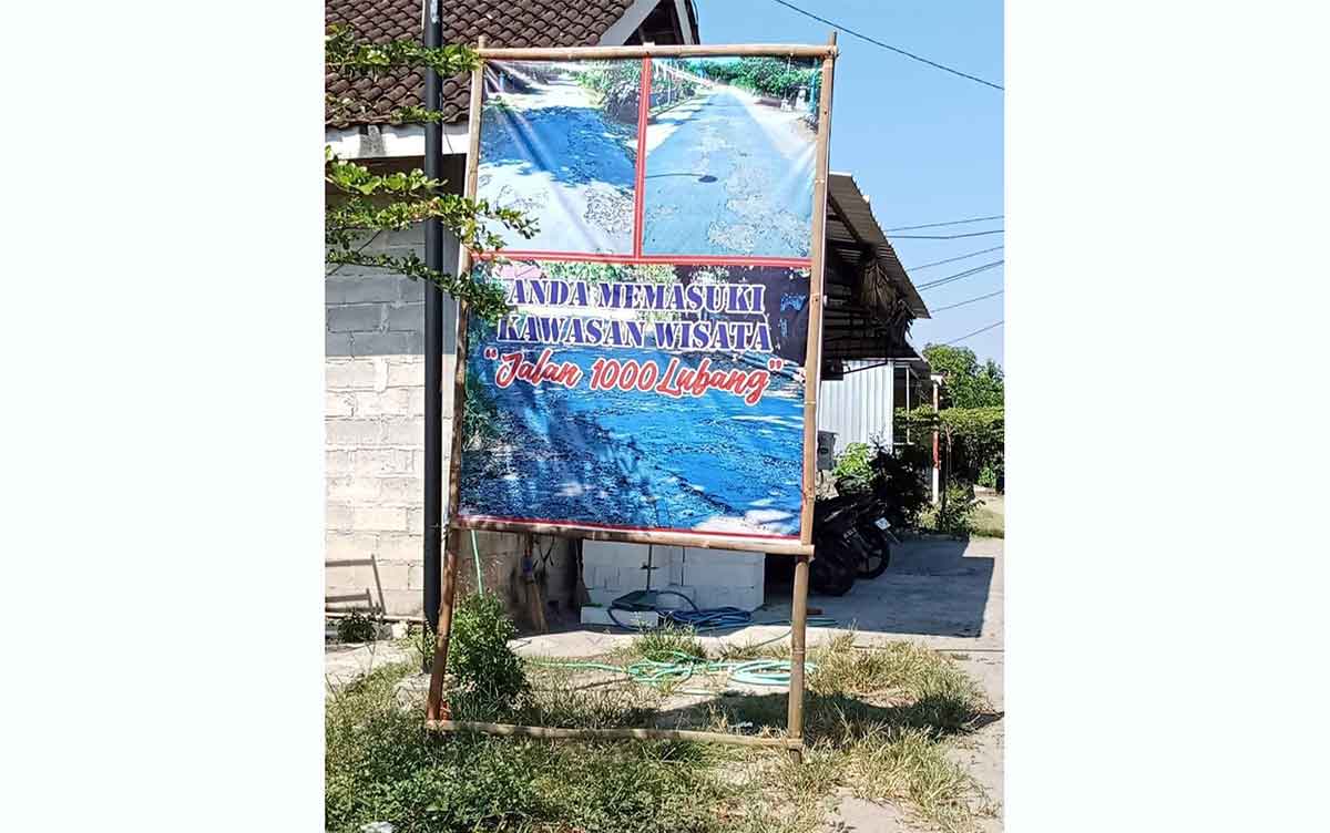 Banner bertuliskan wisata jalan berlubang di Desa Nguntoronadi, Magetan.