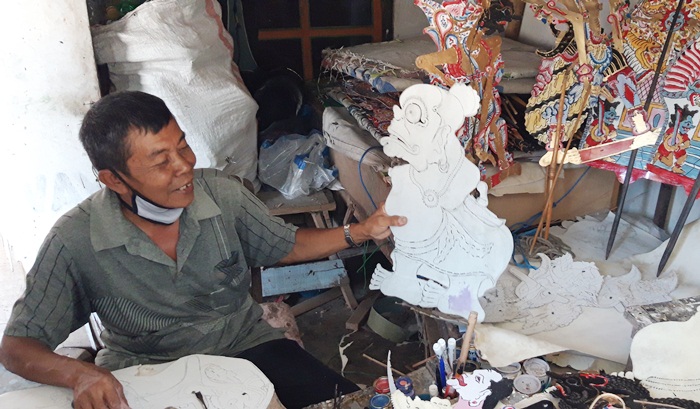 Karmiadi sedang menunjukan wayang kertas hasil tatahannya. foto: MUJI HARJITA/ BANGSAONLINE