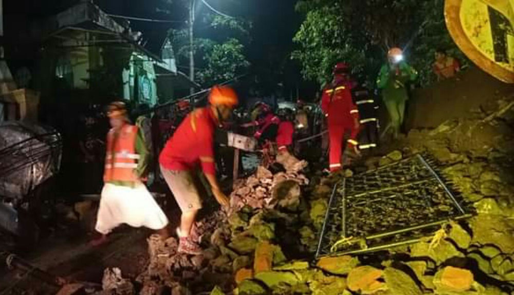 Sejumlah petugas gabungan beserta warga saat bekerja sama mengevakuasi material pagar tembok yang ambrol saat hujan deras di Kota Malang.