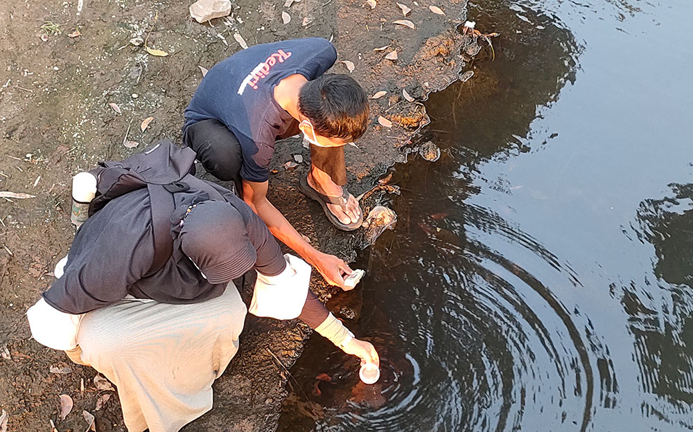 Endang Pertiwi dibantu timnya saat mengambil sampel air Sungai Kresek untuk dibawa ke laboratorium. foto: MUJI HARJITA/ BANGSAONLINE