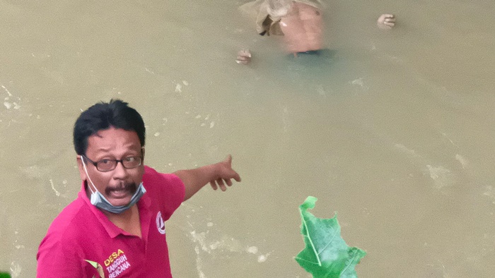Seorang warga sedang menunjuk ke arah mayat yang terapung di sungai. 