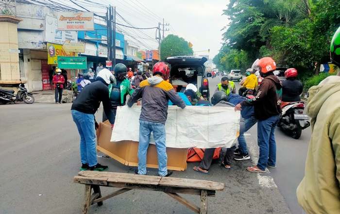 Petugas dibantu warga sedang menutupi jenazah korban kecelakaan akibat tertabrak truk.